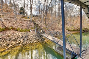 A wooden bridge over a clear stream with a metal railing, surrounded by trees and a rocky path. - Hike & Fish: Lake Keowee Retreat w/ Shared Dock! (Seneca)
