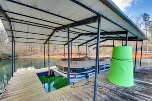 A covered boat dock with a green barrel, a covered boat, and a wooden dock. - Home 11 Mi to Clemson: Lake-view Balcony & Dock! (Seneca)