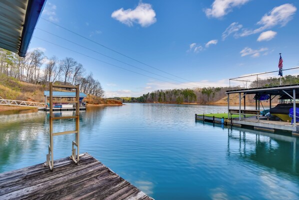 A calm river with a wooden dock, a covered seating area, and a small building with a blue roof. - Home 11 Mi to Clemson: Lake-view Balcony & Dock! (Seneca)