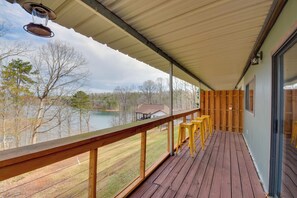 Eine Holzterrasse mit Geländer, einer Hängelampe und Blick auf einen See und Bäume.