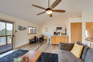 A modern living room with a sofa, a coffee table, a dining area with chairs, a kitchen with a microwave, and a ceiling fan. - Home 11 Mi to Clemson: Lake-view Balcony & Dock! (Seneca)