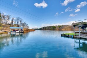 A calm lake with docks, a covered seating area, and a building with a blue roof. - Home 11 Mi to Clemson: Lake-view Balcony & Dock! (Seneca)