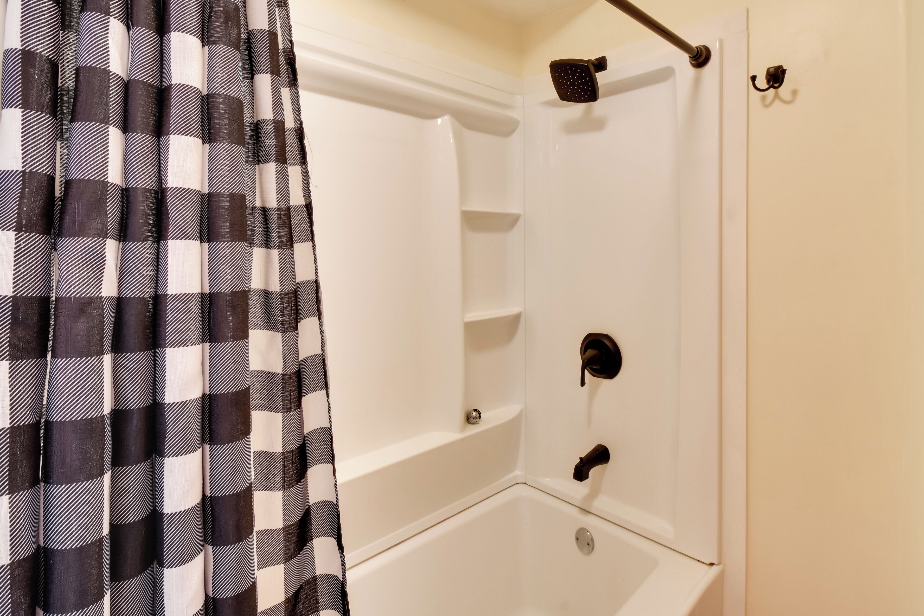 Una doccia d'angolo con tenda a quadri, una vasca da bagno bianca e un soffione.