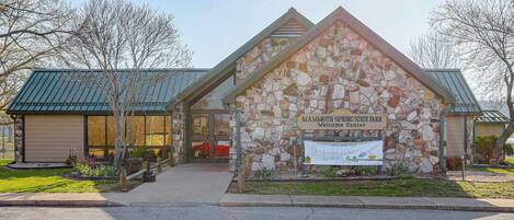 Een gebouw van steen met een bord waarop staat 'Mammoth Spring State Park Welcome Center'.