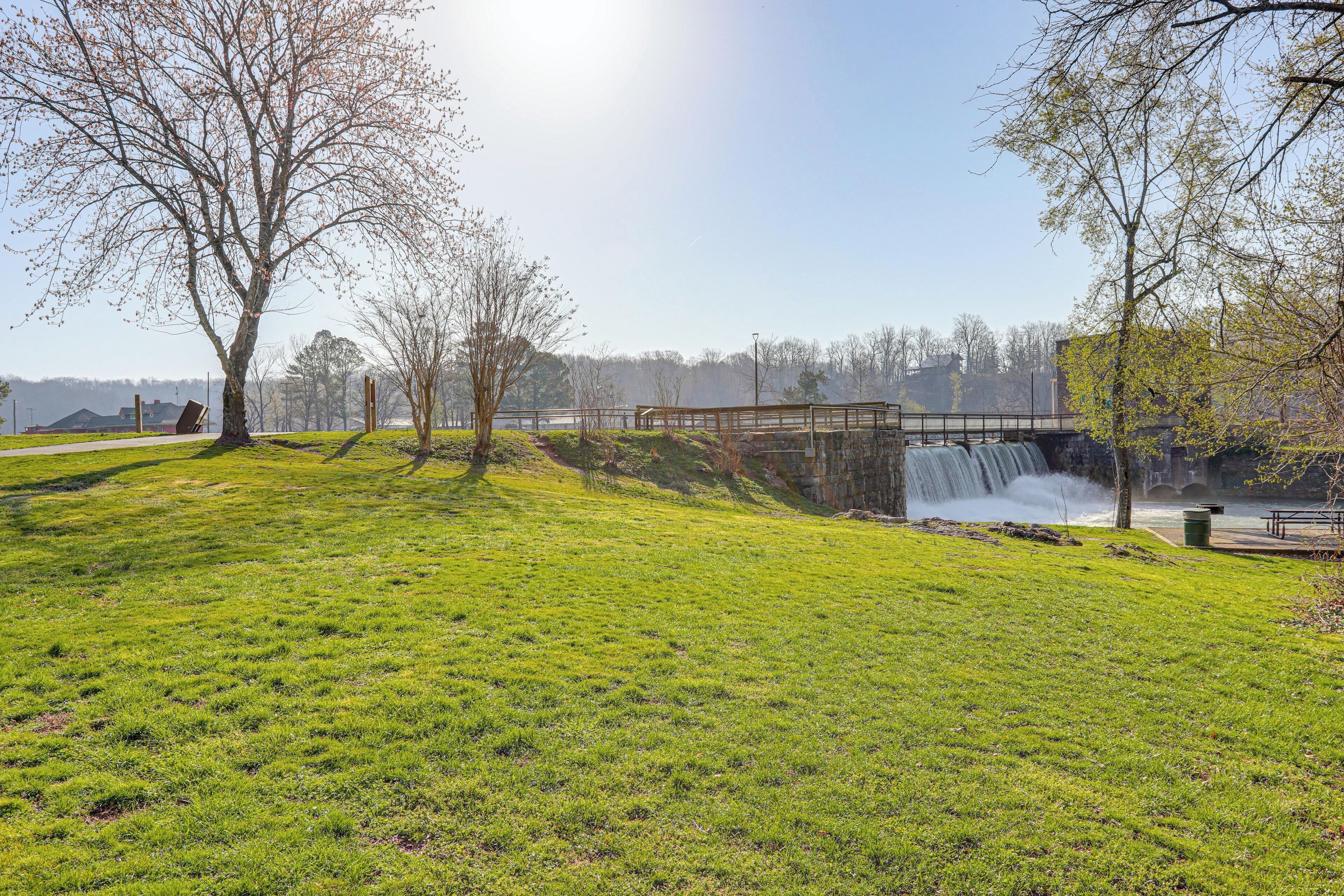 A park with a grassy area, trees, a wooden bridge, and a waterfall.