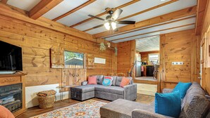 Ein Holzhütten-Interieur mit einem Ecksofa, einem Fernseher, einem Kamin und einem Deckenventilator.