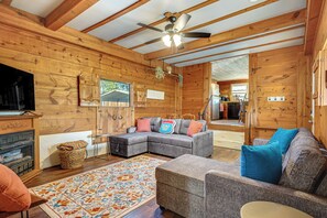 A log cabin interior with a sectional sofa, a television, a fireplace, and a ceiling fan.