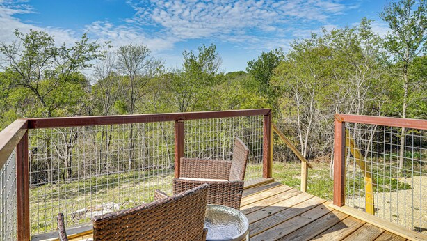 Eine Holzterrasse mit Korbstühlen und einem Tisch, umgeben von einem Drahtzaun, mit Blick auf eine natürliche Landschaft.