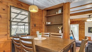 Ein Esszimmer mit Holzboden, einem Tisch, Stühlen, einer Pendelleuchte und einem Fenster.