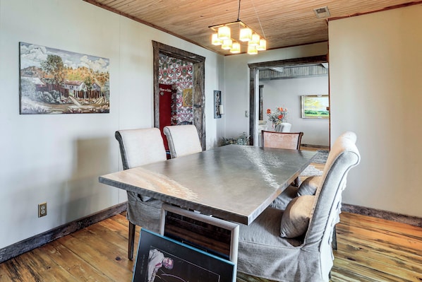 A dining area with a long table, chairs, and a hanging light fixture.