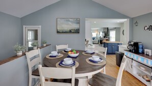 A dining area with a round table set for six, surrounded by white chairs, with a kitchen in the background. - Near Pine Knob, Lakes & Trails! Ortonville Getaway (Ortonville)