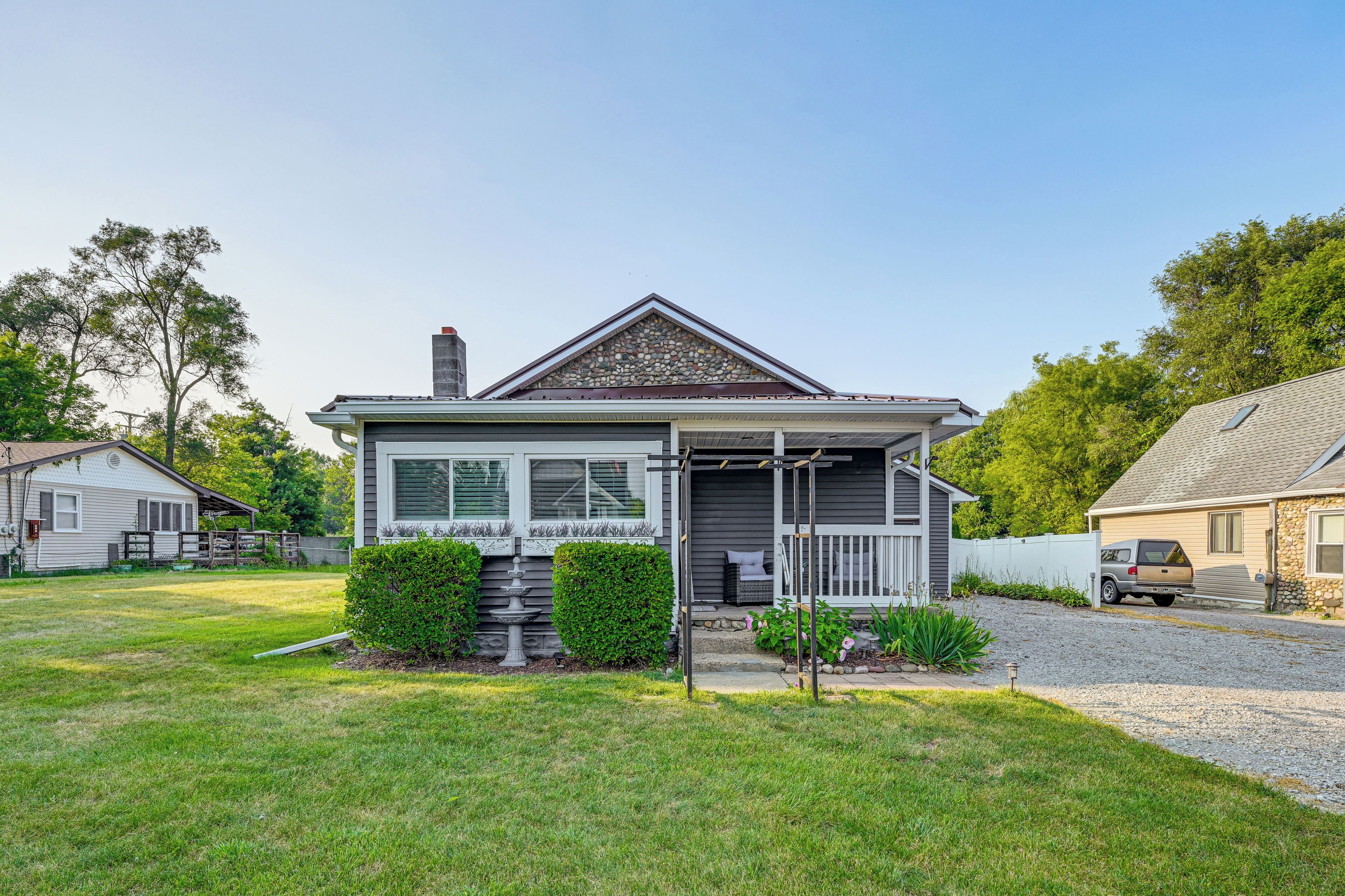 A two-story house with a front porch, a stone chimney, and a well-maintained lawn.