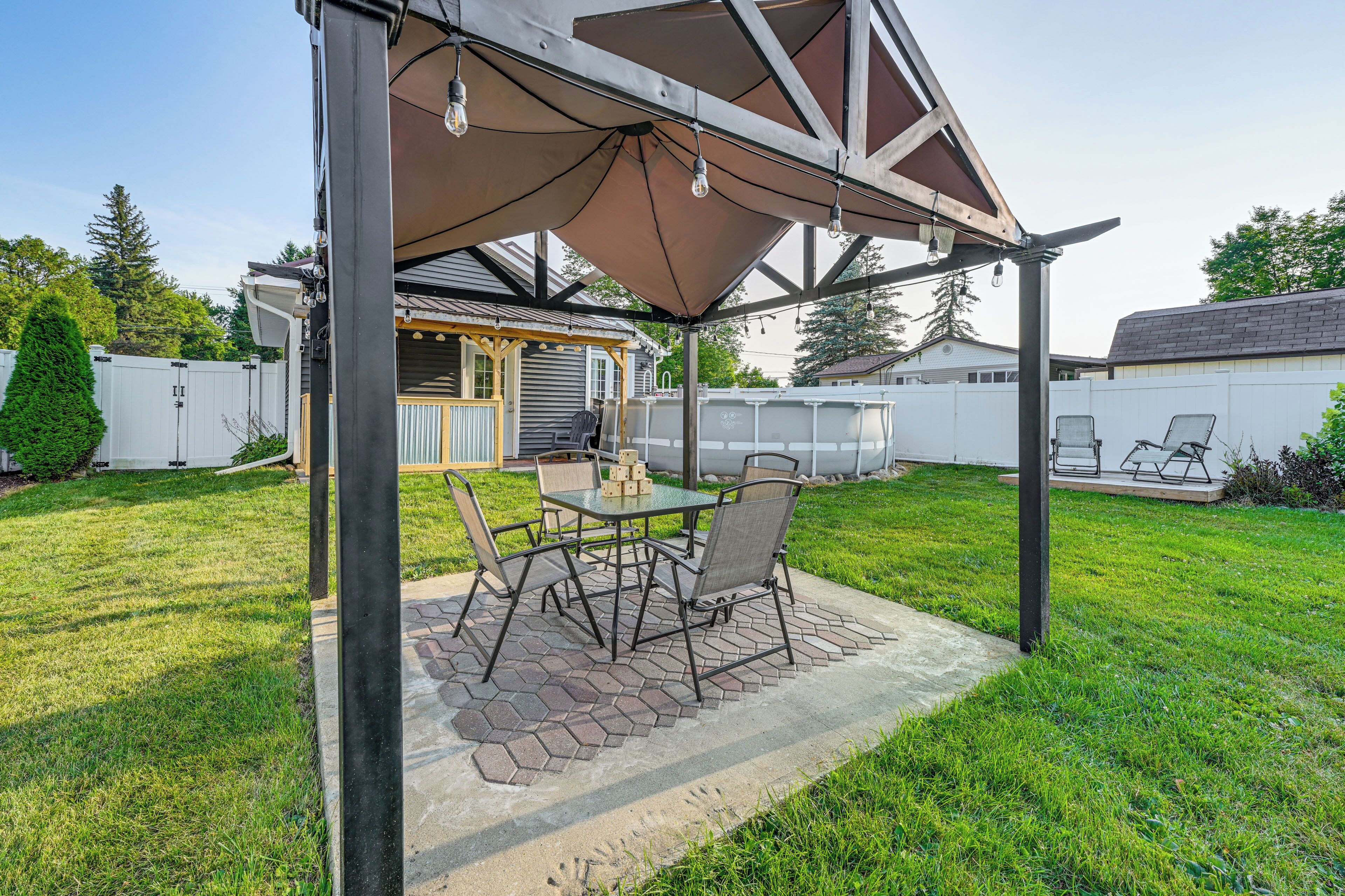 An outdoor patio with a table and chairs, a covered seating area, and a pool in the background.