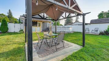 An outdoor patio with a table and chairs, a covered seating area, and a pool in the background.