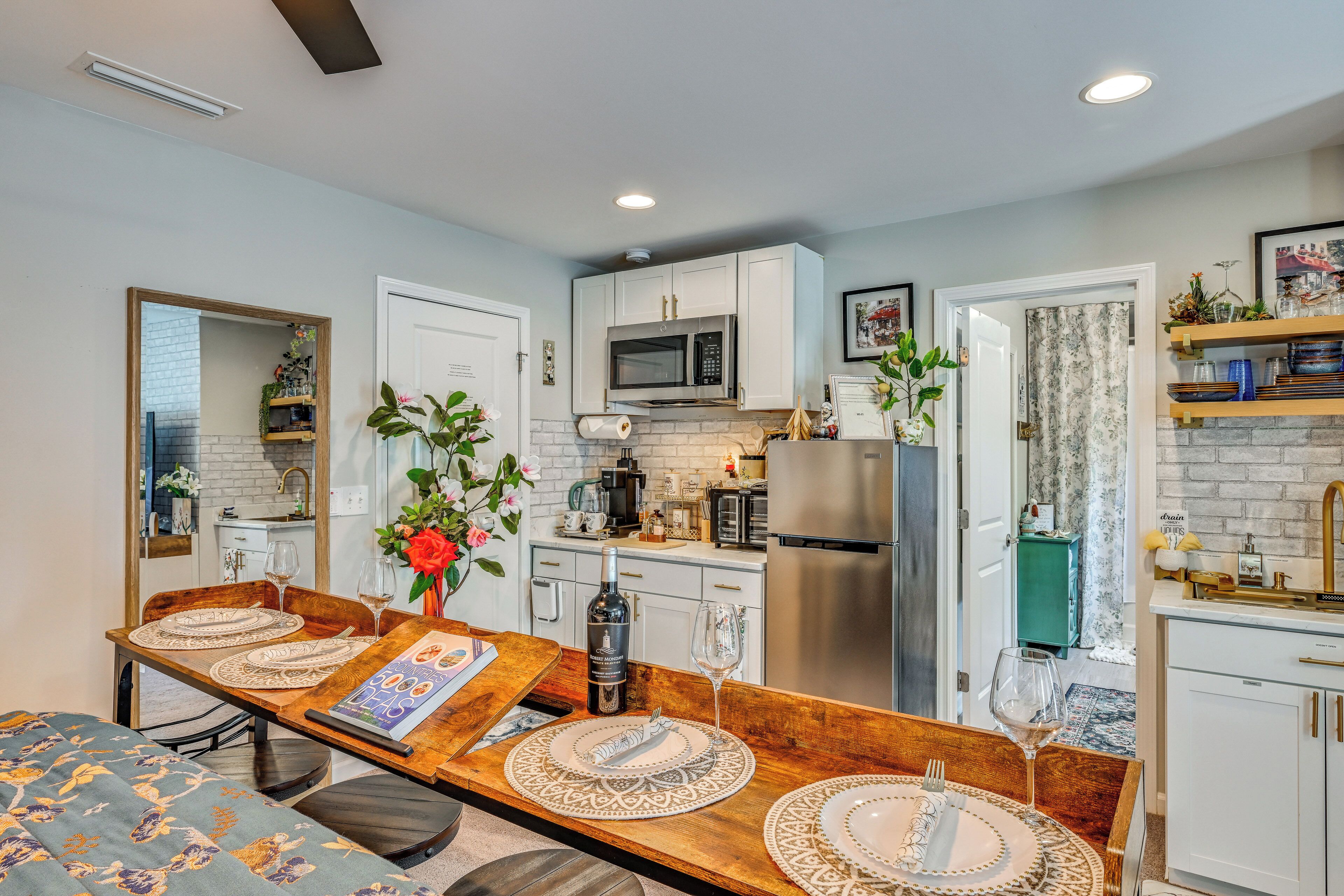 Una cocina moderna con armarios blancos, un refrigerador de acero inoxidable y un comedor con una mesa de madera dispuesta para dos personas.