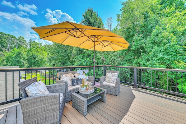 A deck with wicker furniture, a yellow umbrella, and a view of a lush green landscape. - King Studio Near Charlotte Speedway, Ev-l2 Charger (Concord)