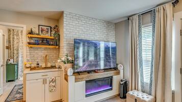 A modern living room with a flat-screen TV mounted on a brick wall, a fireplace with a glass front, and a small seating area.