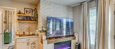 Una sala de estar moderna con un televisor de pantalla plana montado en una pared de ladrillo, una chimenea con frente de vidrio y una pequeña zona de estar.