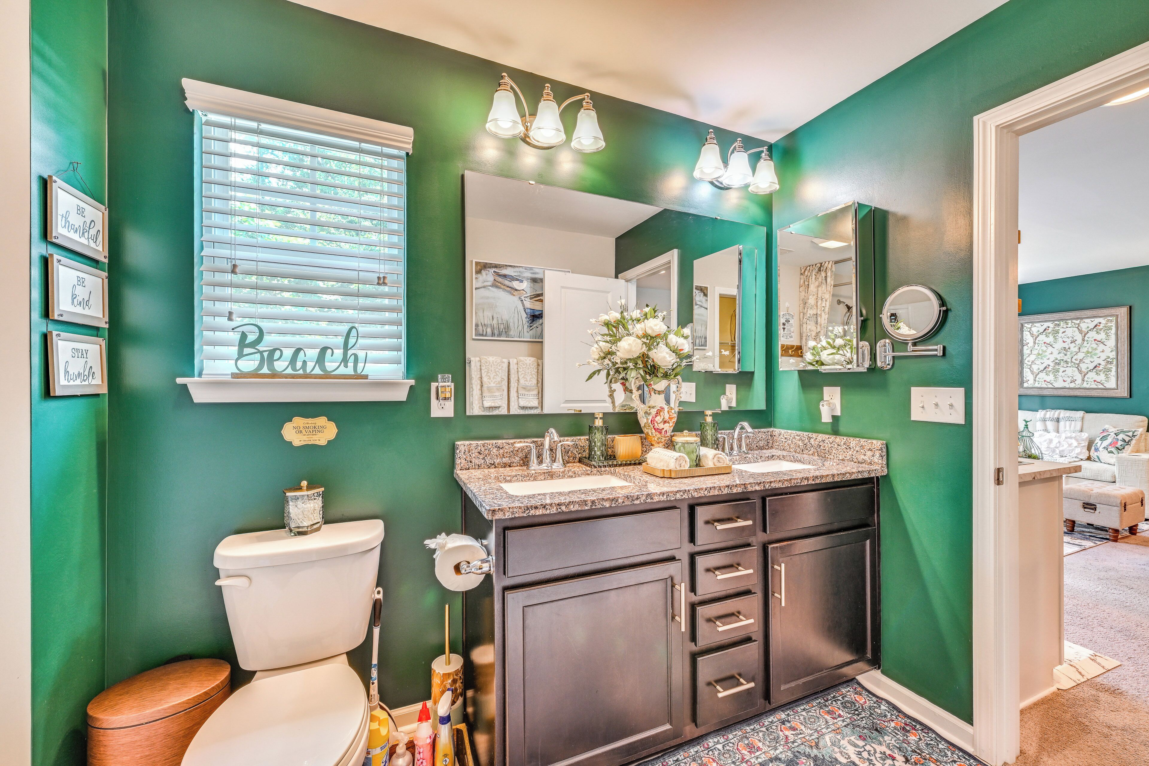 A bathroom with a green wall, a toilet, a sink with a vanity, and a mirror.