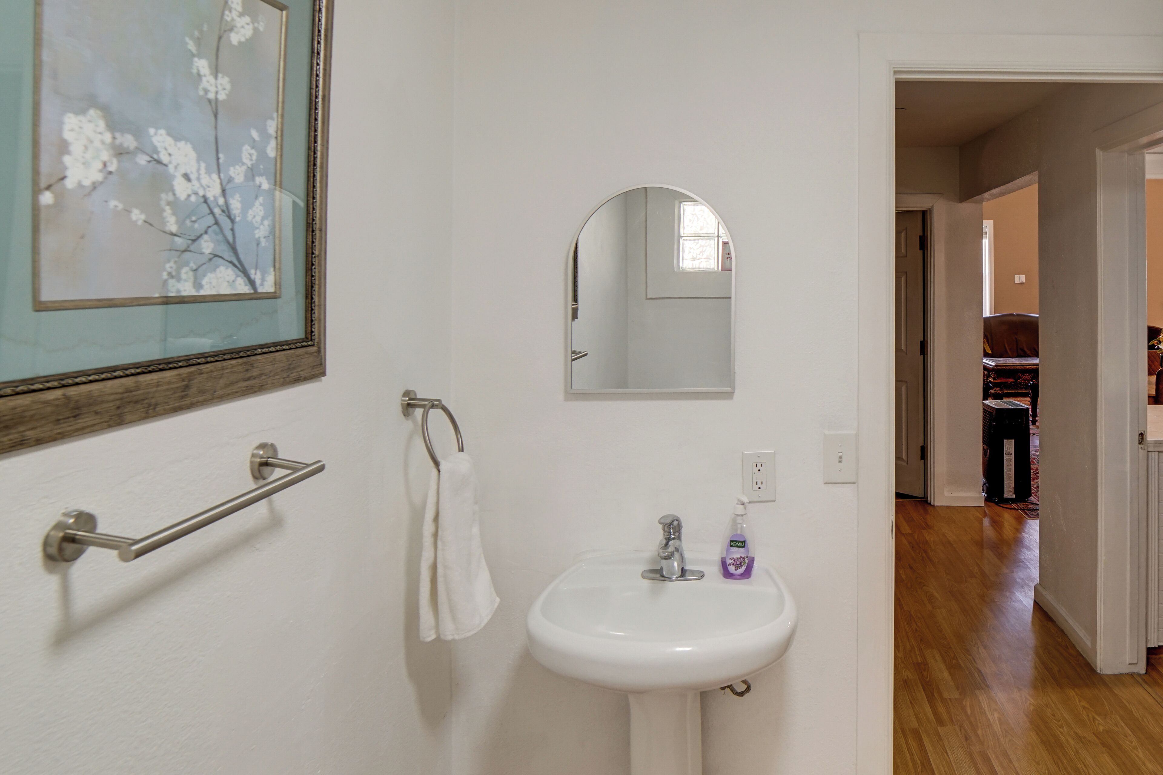 Un baño con un lavabo blanco, un espejo, un perchero para toallas y un cuadro en la pared.