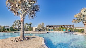 A swimming pool with a wooden pergola, palm trees, and a brick walkway.