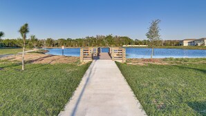 A concrete pathway leading to a wooden bridge over a body of water, surrounded by grass and trees.