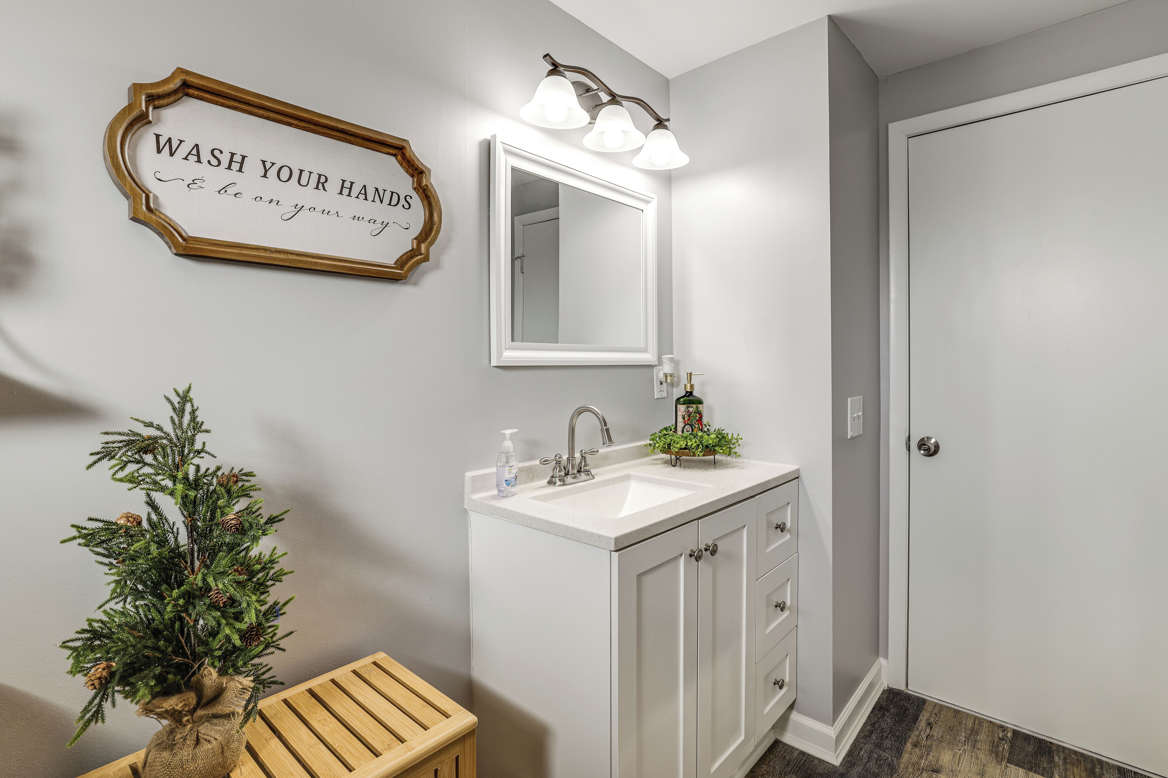Une salle de bain avec un lavabo blanc, un miroir, un panneau décoratif et une petite plante.