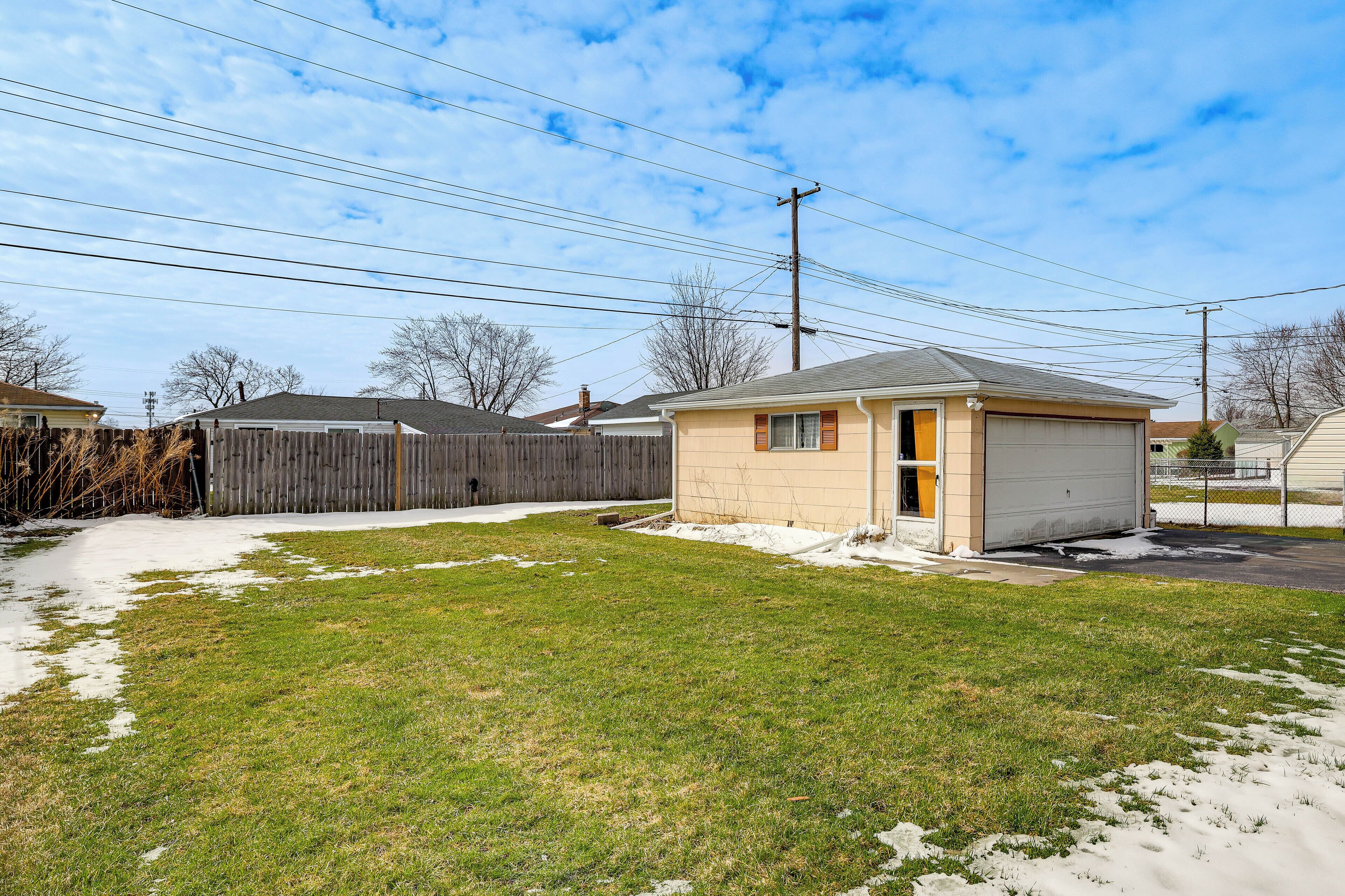 A residential property with a detached garage, a fenced backyard, and a clear sky.