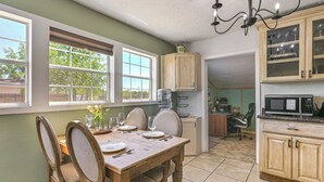 Un coin repas avec une table et des chaises en bois, une cuisine équipée d’armoires et d’un four à micro-ondes, et une vue par la fenêtre.