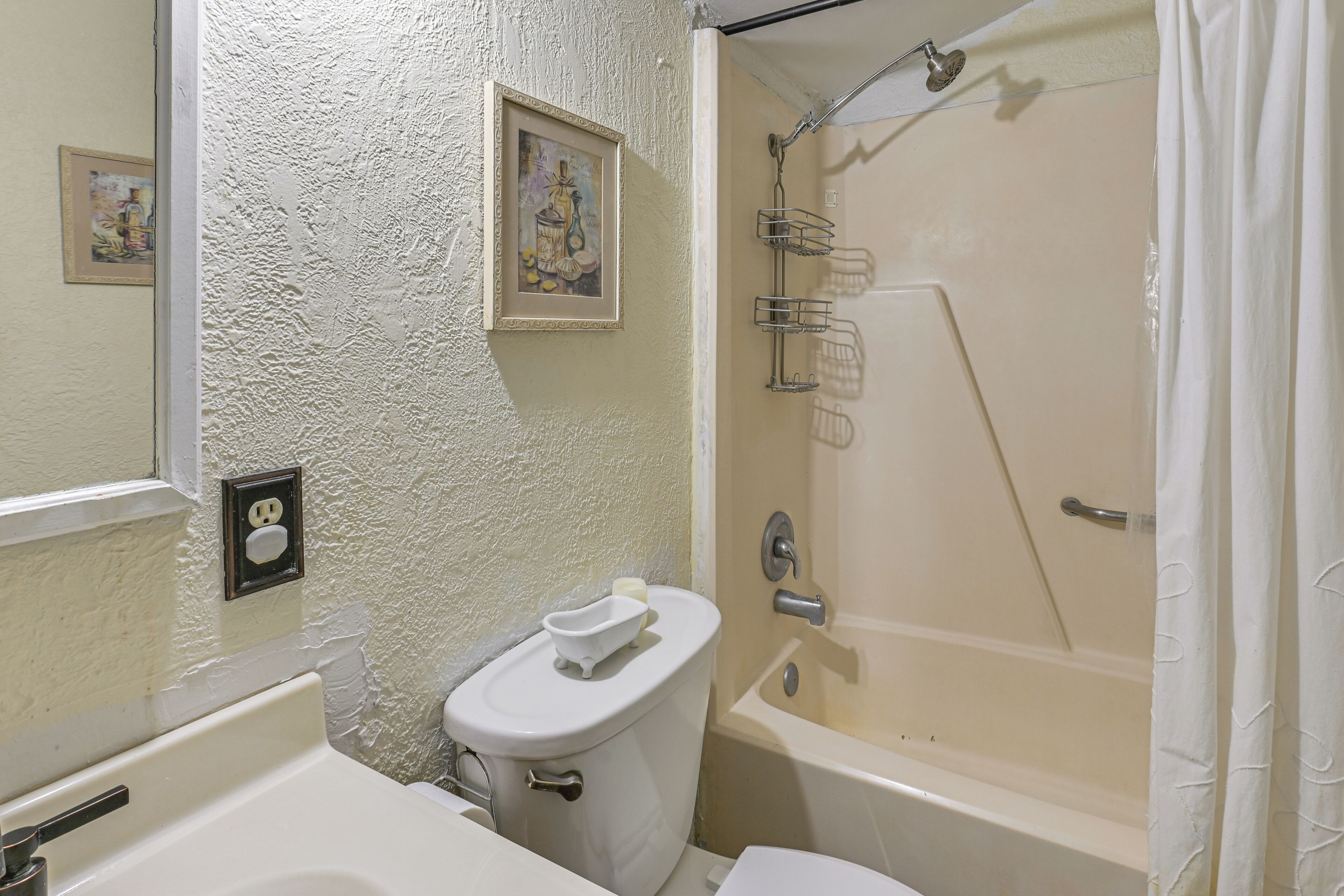 A bathroom with a toilet, sink, bathtub, and shower. There is a framed picture on the wall and a towel on the toilet.