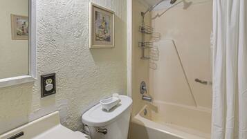 A bathroom with a toilet, sink, bathtub, and shower. There is a framed picture on the wall and a towel on the toilet.