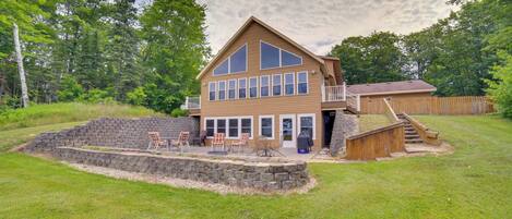 A two-story house with a balcony, a stone retaining wall, and outdoor seating.