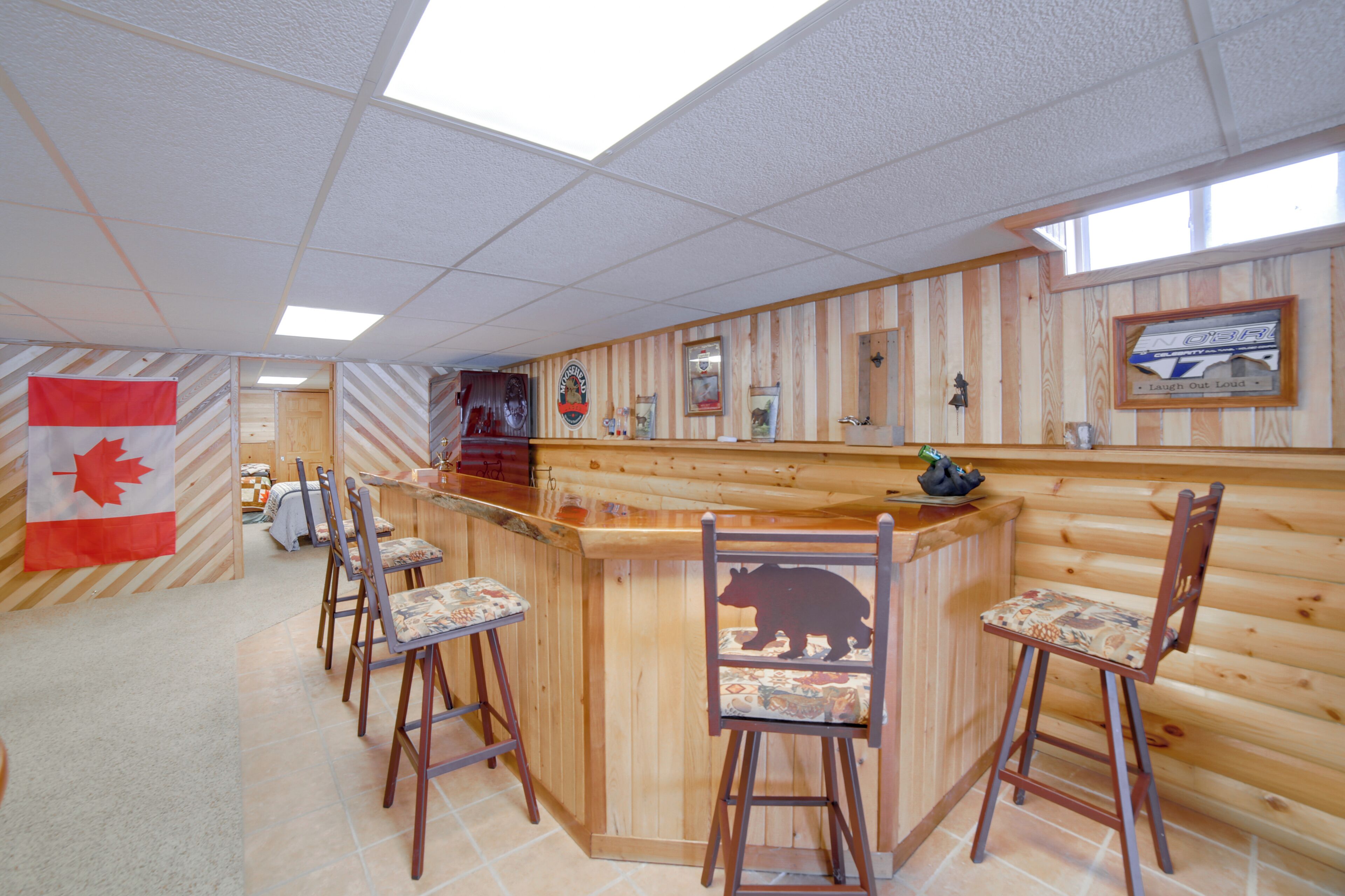 Zona de bar con paneles de madera, una bandera canadiense y un sillón con temática de oso.
