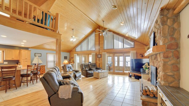A spacious living area with a high ceiling, wooden floors, a stone fireplace, and a dining area with wooden furniture.