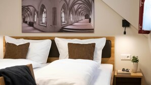 Habitación de hotel con una cama grande, cabecero, mesita de noche con una planta y un cuadro colgado en la pared.