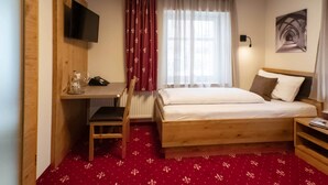 A bedroom with a wooden bed, a desk with a chair, a television mounted on the wall, and a window with curtains. - Comfortable single room with modern furnishings in the heart of Heidenheim (Heidenheim)