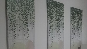 Une salle de bain avec trois tableaux abstraits accrochés au mur, un meuble-lavabo blanc avec un miroir et quelques articles de toilette posés sur le plan de travail.