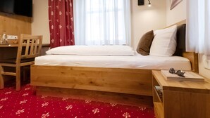 Ein Schlafzimmer mit einem Holzbett, einem Schreibtisch mit Stuhl, einem an der Wand montierten Fernseher und einem Fenster mit Vorhängen.