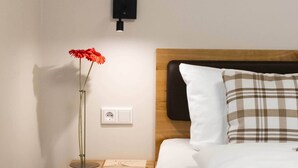 Ein Hotelzimmer mit einem hölzernen Kopfteil, einem Nachttisch mit Buch und Blumenvase, einer Steckdose und einer Wandleuchte.