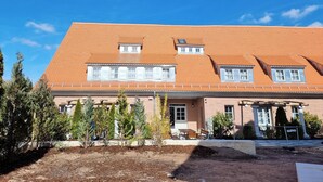 A two-story building with a red-tiled roof, multiple windows, and a front porch with outdoor seating.