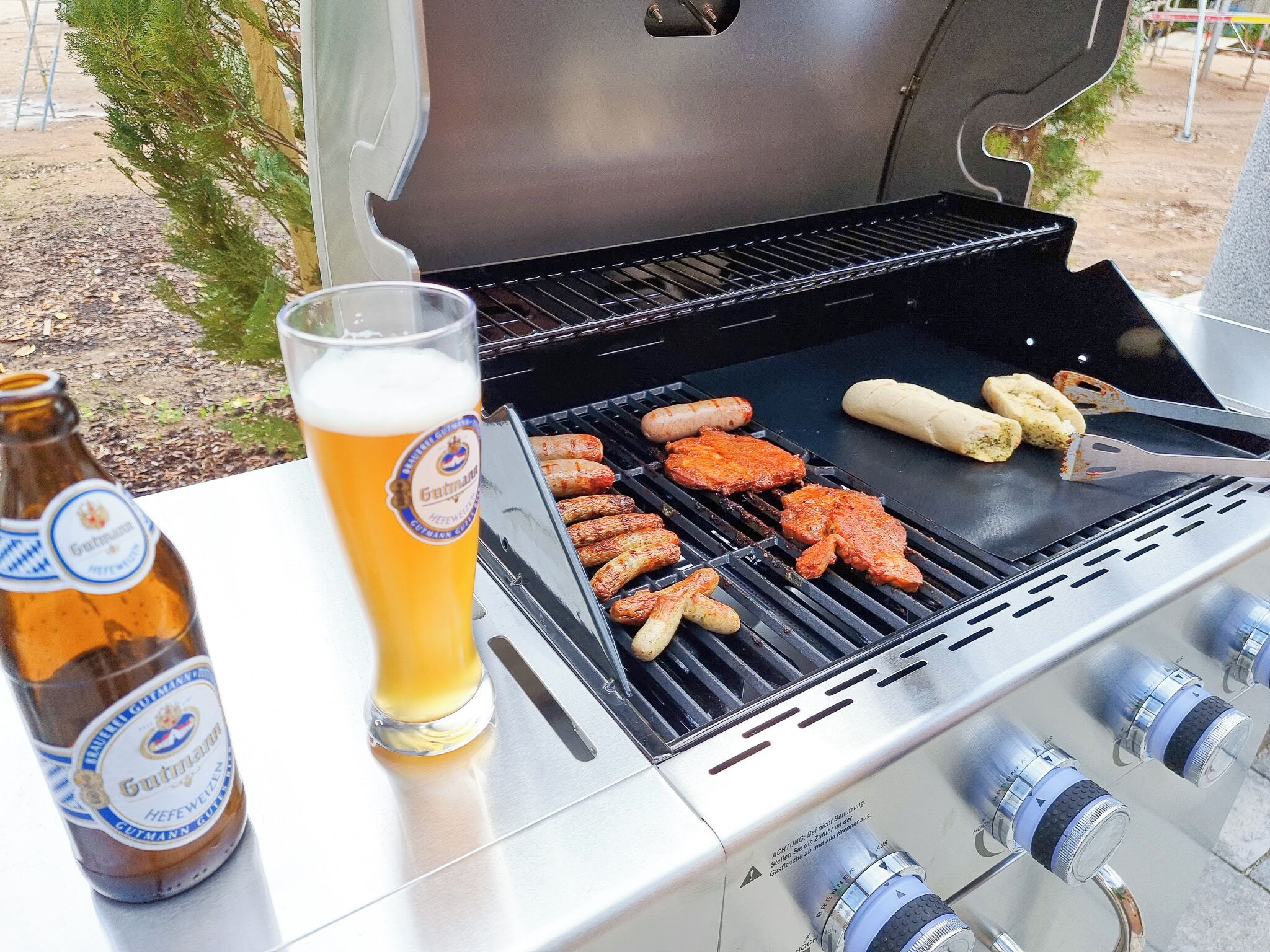 Una parrilla con salchichas y pollo, una botella de cerveza y un vaso de cerveza.