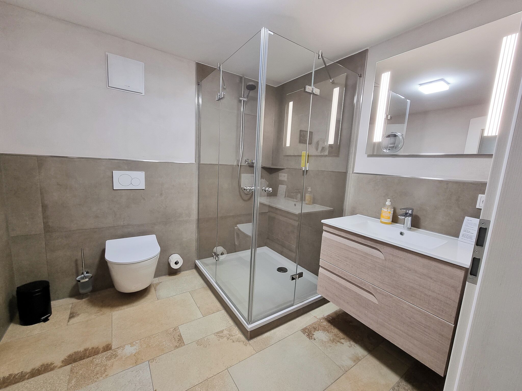 Une salle de bain moderne avec une douche à parois de verre, des toilettes blanches, un meuble-lavabo avec un miroir et un évier.