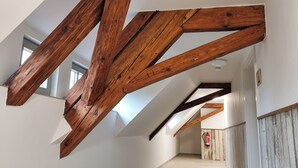 Un couloir aux poutres apparentes, aux murs blancs et au plancher en bois.