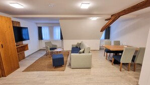 Een moderne woonkamer met een flatscreen televisie, een bank, een eettafel met stoelen en een houten kast.