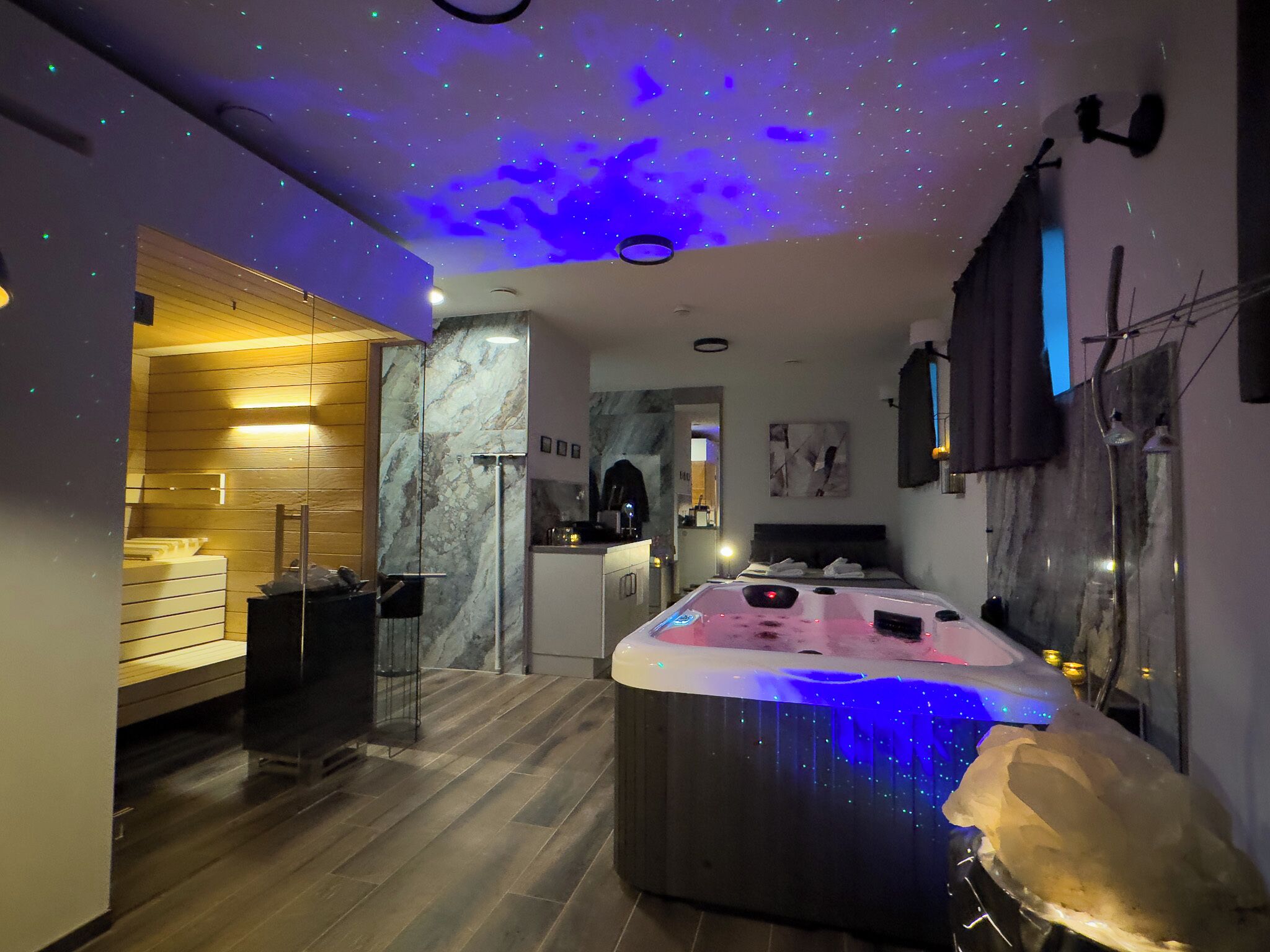 Ein modernes Badezimmer mit Marmorwand, einem Holzbadezimmermöbel und einer Decke mit Sternenprojektion.