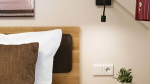 A hotel room with a bed, a nightstand with a plant, a book, and glasses, a power outlet, and a wall-mounted light. - Comfortable double room in the historic town center of Heidenheim (Heidenheim)
