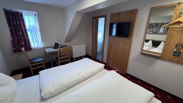 Ein Hotelzimmer mit zwei Betten, einem Schreibtisch mit Stuhl, einem Fernseher, einem Spiegel und einem Fenster mit Vorhängen.