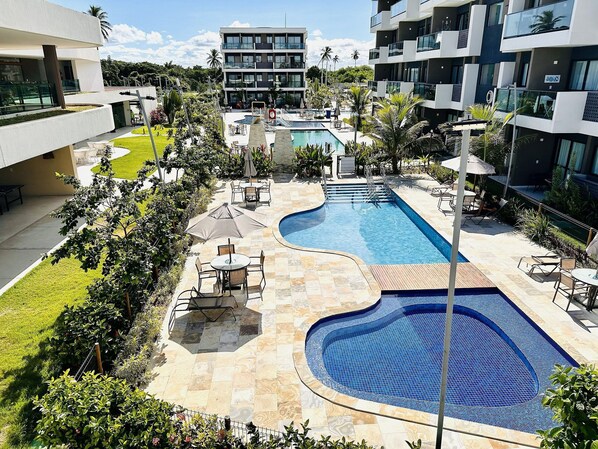 A modern hotel with a swimming pool, outdoor seating, and lush landscaping. - Makia Beach Experience - Muro Alto (Ipojuca)