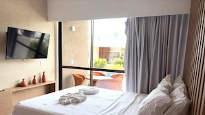 Hotellihuone, jossa on sänky, taulutelevisio, ikkuna verhoilla ja näkymä ulos.