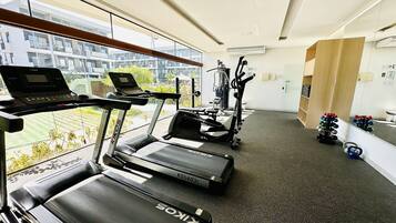 Une salle de sport équipée de tapis de course, d’un ordinateur portable posé sur un banc et de matériel d’exercice.